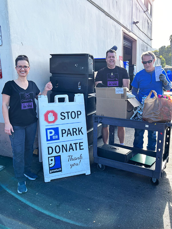 Image of two men and a woman standing outside the Goodwill donation area next to a cart of donated household items.