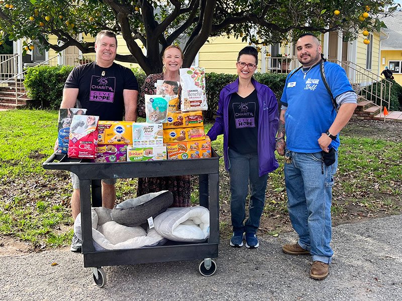 Image of two men and two women standing outside next to a cart full of pet food and beds.  CharityRx Spreading Hope Through Donations