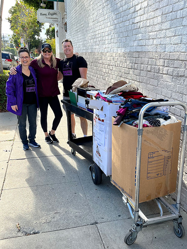 Image of two women and a man standing outside next to a cart of donated clothing and household items. CharityRx Spreading Hope Through Donations