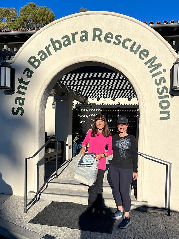 Image of two women standing outside the Santa Barbara Rescue Mission holding bags of donated items.