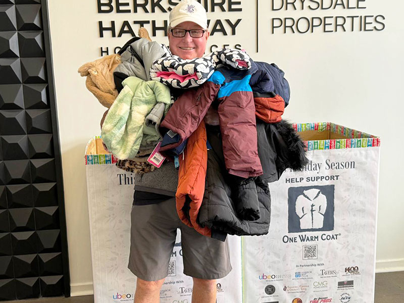 Image of a smiling man holding a huge armful of coats to be donated to One Warm Coat. CharityRx Spreading Hope Through Donations
