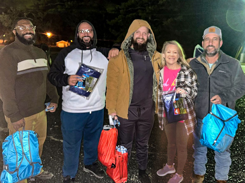 Image of four men and one woman standing in a row at night. Each person is holding a backpack or tarp.