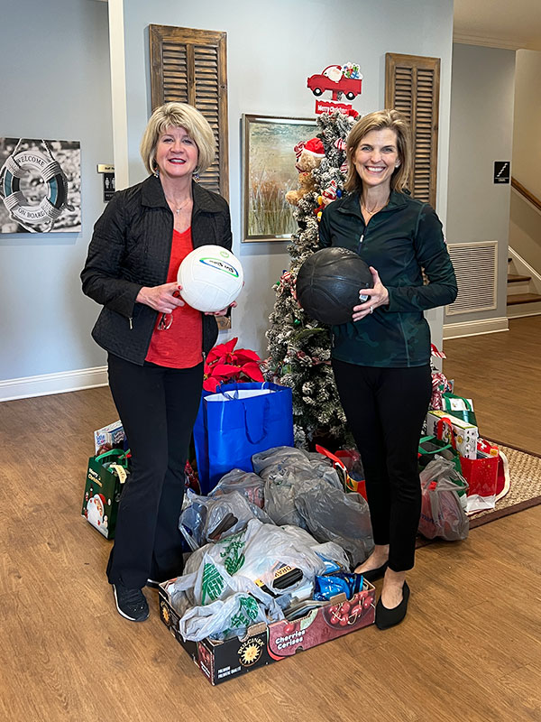 Image of two women standing next to a Christmas tree with gifts at their feet. Each woman is holding a soccer ball. CharityRx Spreading Hope Through Donations
