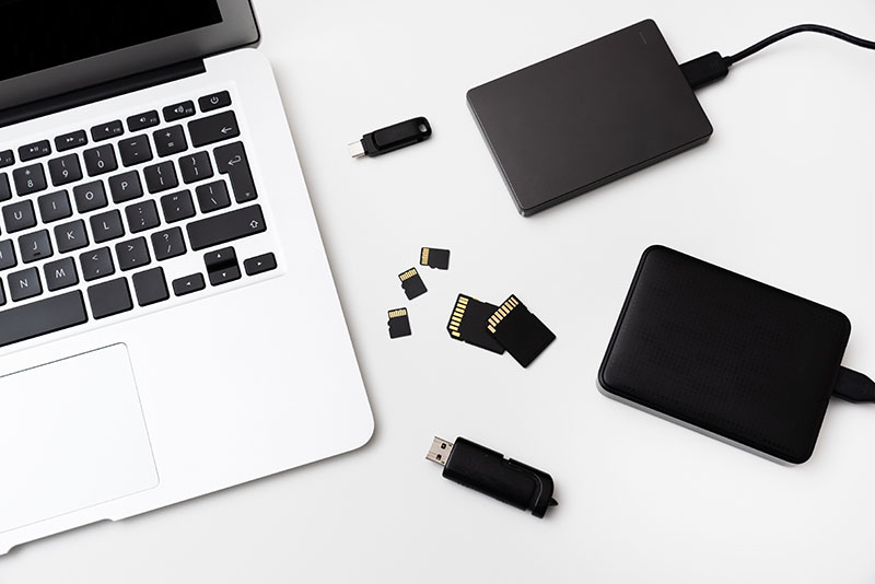 Image of electronic storage devices, a laptop, external hard drives, thumb drives, and memory cards.