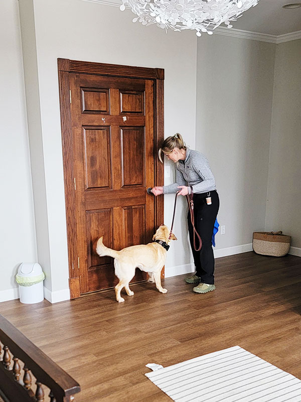Image: A young woman detective holds the leash of Charity, the K9 Crusader and points to the doorknob of a wooden door.